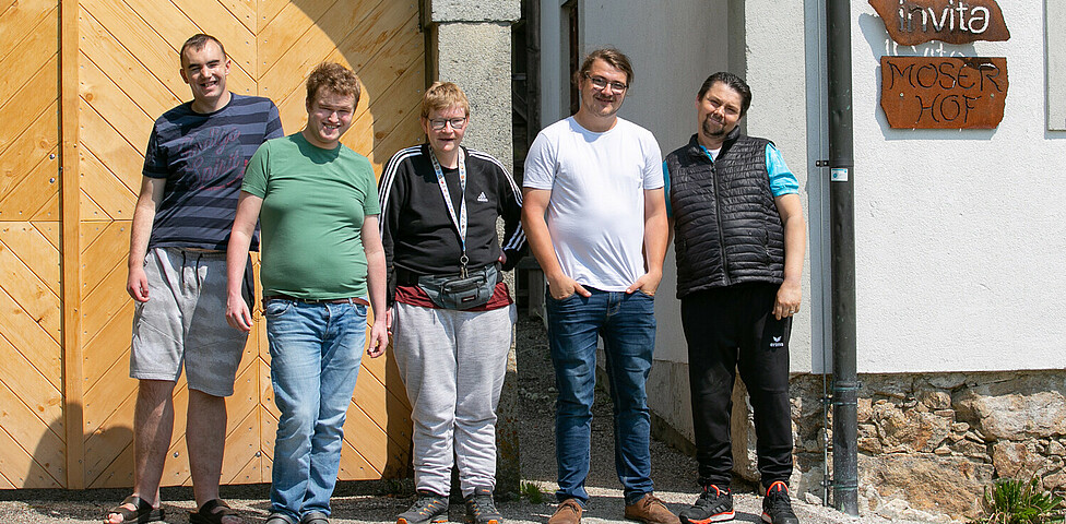 Fünf Männer stehen vor einem hellbraunen Holztor und einer kleineren Tür.