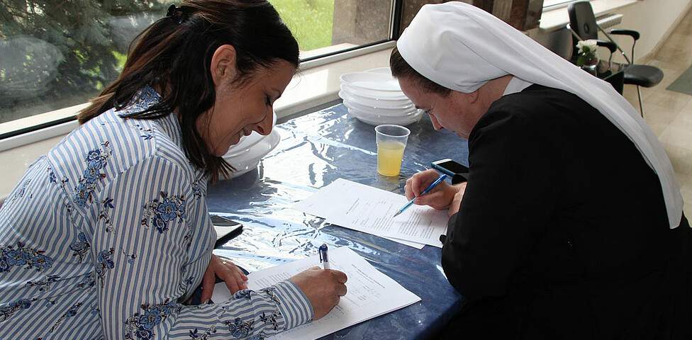 Zwei Frauen sitzen an einem Tisch und schreiben auf ein Blatt Papier