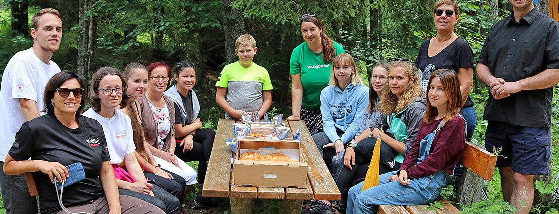 Ein Gruppenfoto. Jugendliche sitzen im Wald ein einen Tisch.