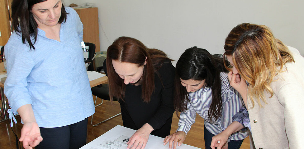 Vier Frauen stehen um einen Tisch und arbeiten an einem Plakat