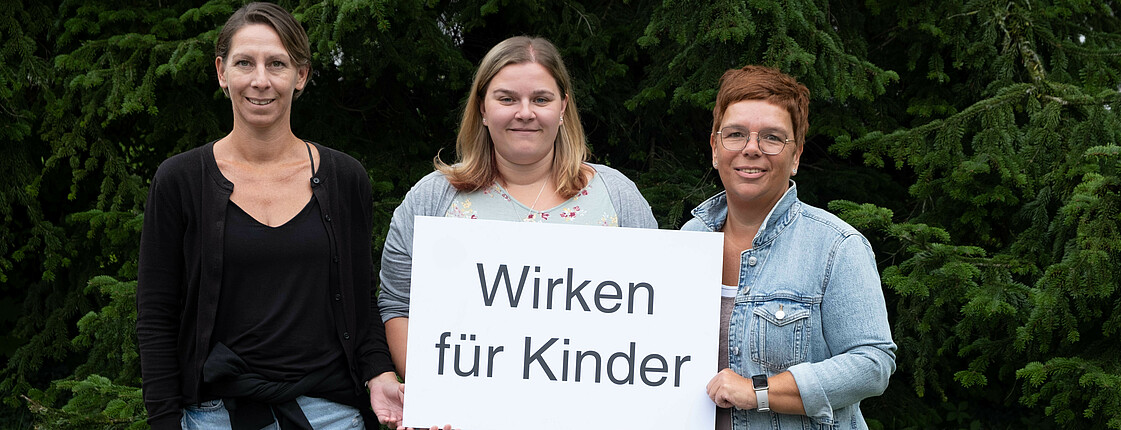 Drei Frauen halten ein Schild mit der Aufschrift: Wirken für Kinder